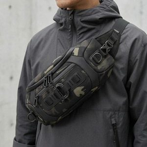 May include: A black and camouflage sling bag with multiple zippered compartments and a shoulder strap. The bag features a tactical design with a buckle closure and a D-ring attachment. The bag is worn across the chest.