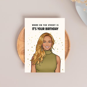 May include: Birthday greeting card with an illustration of a woman with blonde hair and a green top. The text on the card reads "WORD ON THE STREET IS IT'S YOUR BIRTHDAY". The card is on a wooden plate.