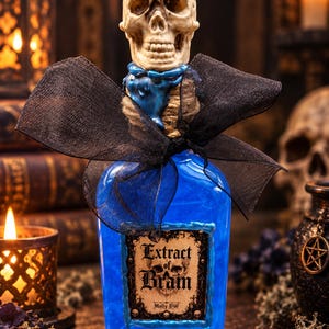 Könnte beinhalten: Eine klare Glasflasche gefüllt mit leuchtend blauer Flüssigkeit, gekrönt von einem realistischen beigen Totenkopf-Verschluss. Der Flaschenhals ist mit Schnur umwickelt und mit einer schwarzen, transparenten Schleife versehen. Das Etikett trägt die Aufschrift Extract of Brain von Molly DW.