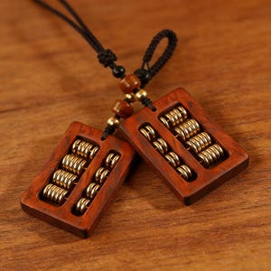 May include: Two wooden abacus pendants with gold-colored beads and a black cord. The rectangular frames are a rich, reddish-brown color. The abacuses are a traditional tool for calculation.