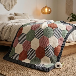 May include: A colorful knitted blanket with a geometric pattern of hexagons in various colors, including red, green, white, and gray. The blanket is draped over a bed, showcasing its design and texture. The blanket's dimensions are approximately 60 inches by 50 inches.
