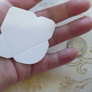 May include: A white folded card envelope, approximately the size of a US quarter, is held in a hand.