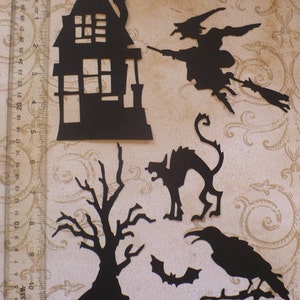 Op de afbeelding: Zwarte papieren uitsnijdingen van Halloween-thema's, waaronder een huis, een heks op een bezem, een kat, een boom, een vleermuis en een raaf.