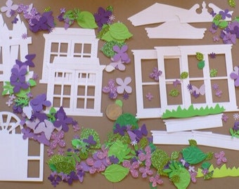 Könnte beinhalten: Ein Set aus weißen Papierschnitten zum Scrapbooking oder Kartenbasteln. Das Set enthält verschiedene Formen, darunter Fenster, Zäune und ein Vogelhaus. Die Ausschnitte sind mit grünen und violetten Papierblumen verziert.