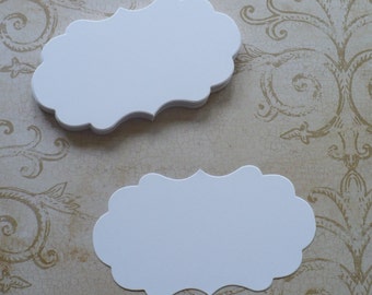 May include: Two white, blank, scalloped-edge gift tags. The tags are made of cardstock and have a slightly textured surface.