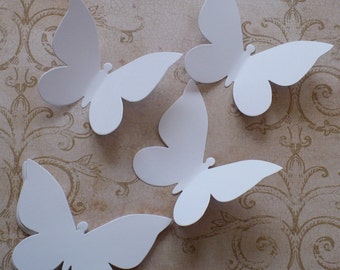 Könnte beinhalten: Vier weiße Papier-Schmetterlinge, in einer einfachen Form ausgeschnitten, sind auf einem gemusterten Hintergrund angeordnet. Die Schmetterlinge sind alle in die gleiche Richtung ausgerichtet, mit ausgebreiteten Flügeln.