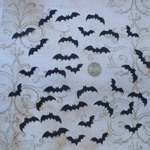 May include: A collection of black paper bats scattered on a patterned surface. The bats are various sizes and shapes, creating a festive Halloween atmosphere.