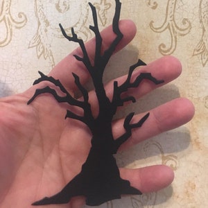 Op de afbeelding: Zwarte silhouet van een kale boom met veel takken. De boom is uit papier geknipt en wordt in een hand gehouden.