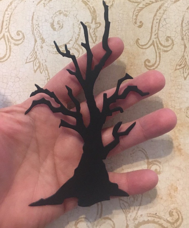 Op de afbeelding: Zwarte silhouet van een kale boom met veel takken. De boom is uit papier geknipt en wordt in een hand gehouden.