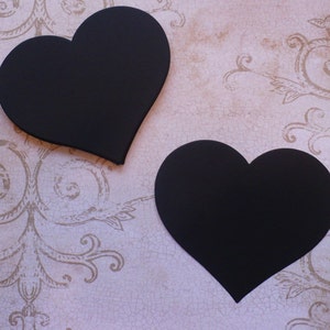 May include: Two black heart-shaped chalkboard signs on a white background with a decorative pattern.