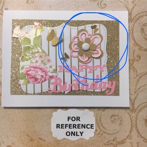 May include: A handmade card with a gold glitter background and a pink and white paper flower. The card says "Happy Birthday" in pink letters.