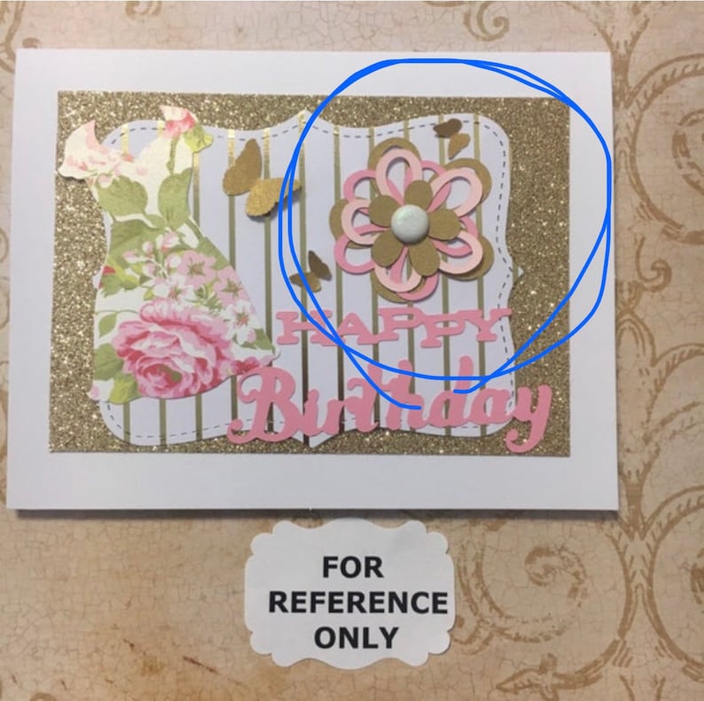 May include: A handmade card with a gold glitter background and a pink and white paper flower. The card says "Happy Birthday" in pink letters.