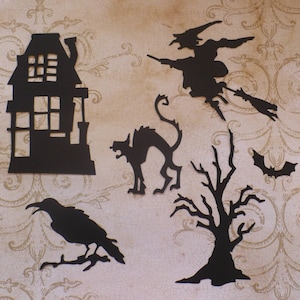 Op de afbeelding: Zwarte papieren uitsnijdingen van een spookhuis, een heks die op een bezem vliegt, een kat, een kale boom en een vleermuis. Deze uitsnijdingen zijn perfect voor Halloween-decoraties.