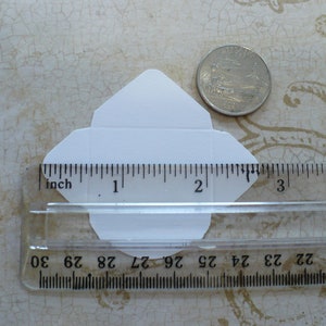 May include: A white envelope measuring 2 inches in length and 1.5 inches in width, next to a ruler and a US quarter.