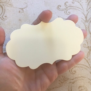 K&ouml;nnte beinhalten: Eine leere, cremefarbene Karte mit gewelltem Rand, die in einer Hand gehalten wird. Die Karte ist aus dickem Papier und hat eine glatte Oberfl&auml;che.