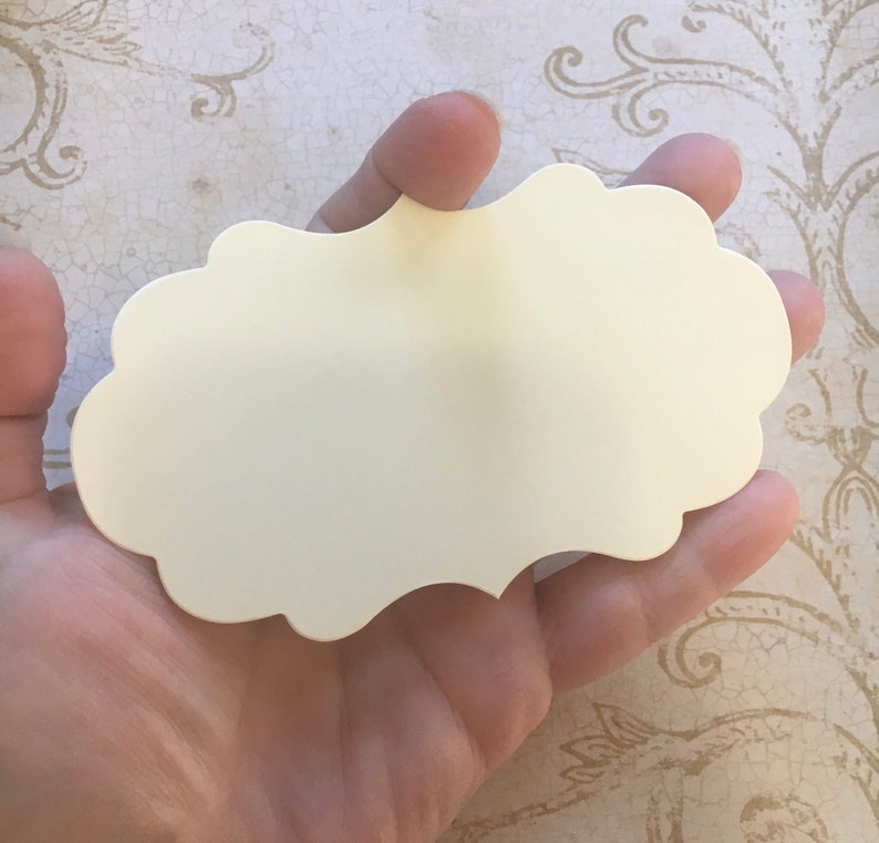 K&ouml;nnte beinhalten: Eine leere, cremefarbene Karte mit gewelltem Rand, die in einer Hand gehalten wird. Die Karte ist aus dickem Papier und hat eine glatte Oberfl&auml;che.