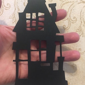 Op de afbeelding: Zwarte papieren uitsnede van een huis met ramen en een schoorsteen. Het huis is een eenvoudige silhouet zonder details.