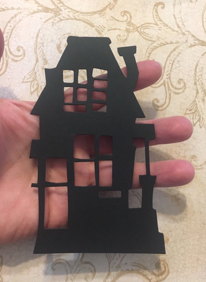 Op de afbeelding: Zwarte papieren uitsnede van een huis met ramen en een schoorsteen. Het huis is een eenvoudige silhouet zonder details.
