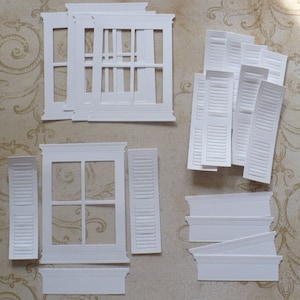 May include: White paper craft die cuts for a window and shutters. The window die cut has a frame and a 6-pane window. The shutters are made of individual slats. There are also die cuts for a window sill and a window header.