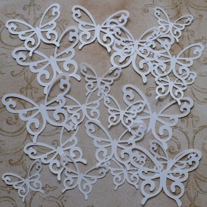 May include: A collection of white paper butterfly cutouts with intricate wing designs. The butterflies vary in size and are arranged on a patterned background, creating a delicate and artistic display. Ideal for crafting and scrapbooking.
