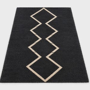 May include: A rectangular area rug featuring a deep charcoal black base with a central vertical pattern of interconnected beige diamond shapes. The rug has a thick, textured pile surface that creates a soft appearance across the entire piece.