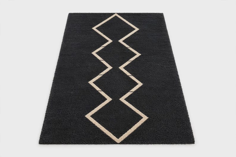 May include: A rectangular area rug featuring a deep charcoal black base with a central vertical pattern of interconnected beige diamond shapes. The rug has a thick, textured pile surface that creates a soft appearance across the entire piece.