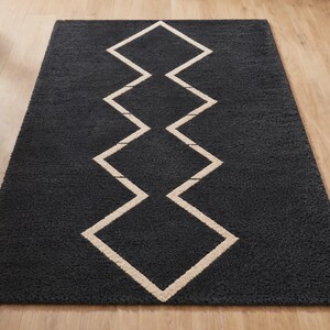 May include: A rectangular area rug featuring a deep charcoal gray pile with a central geometric pattern composed of interconnected white diamond shapes arranged in a vertical line, creating a bold contrast against the dark textured surface.