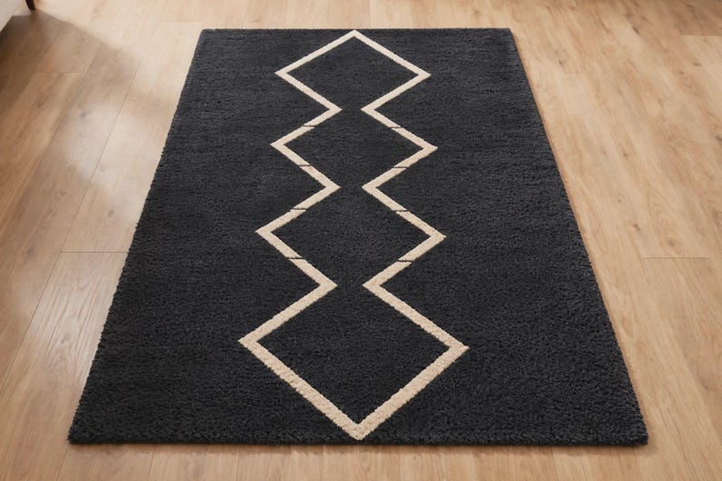 May include: A rectangular area rug featuring a deep charcoal gray pile with a central geometric pattern composed of interconnected white diamond shapes arranged in a vertical line, creating a bold contrast against the dark textured surface.