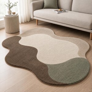 May include: An irregular, cloud-shaped area rug featuring a textured, tufted surface. The design consists of large, flowing color-blocked sections in shades of dark brown, cream, light beige, and muted sage green, creating a soft, organic aesthetic.