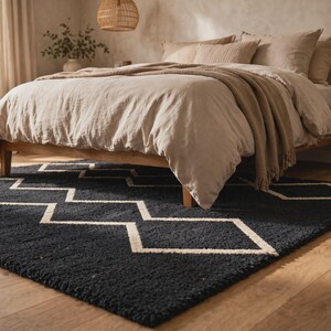 May include: A rectangular area rug featuring a deep charcoal black base with a contrasting white geometric zigzag pattern. The rug has a thick, textured pile and is positioned on a light-toned wooden floor beneath a wooden bed frame.