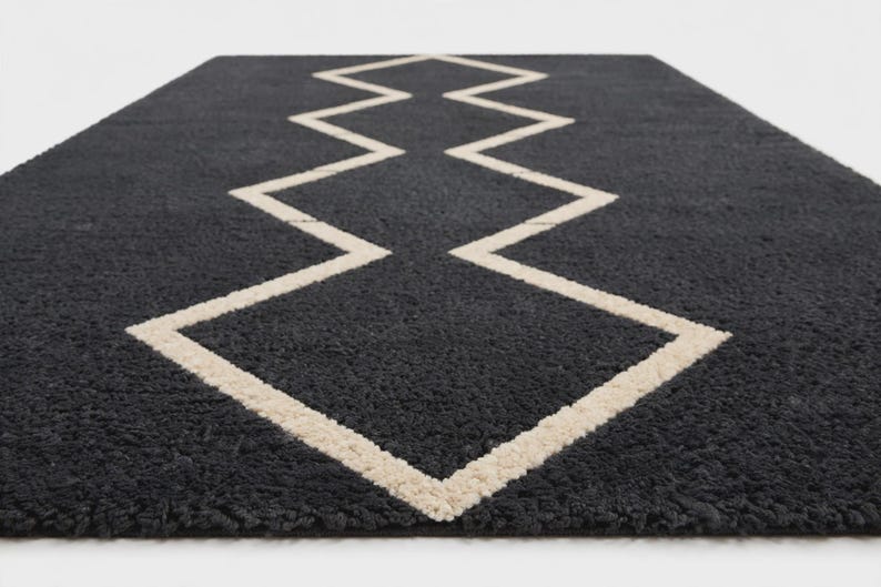 May include: A rectangular area rug featuring a deep charcoal gray, high-pile textured surface. A prominent, continuous cream-colored line forms a sharp, symmetrical zigzag pattern that runs vertically through the center of the rug.
