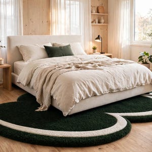 May include: A large, cloud-shaped area rug featuring a deep forest green center with a thick, curved cream-colored border. The rug has a textured, tufted pile surface and is positioned underneath a bed frame in a bedroom setting.