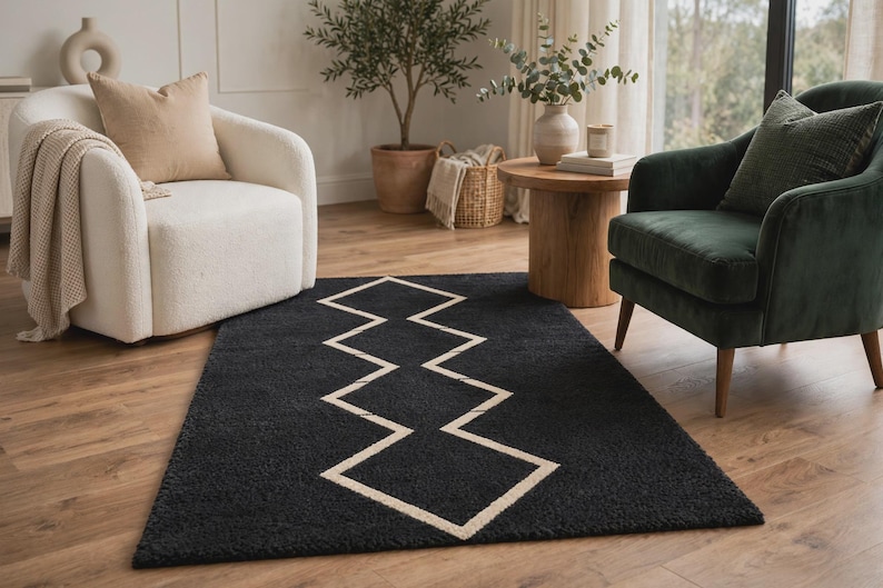 May include: A rectangular area rug featuring a deep black, textured pile surface with a prominent, centered geometric pattern composed of thin, light beige lines that form a continuous, repeating zigzag or diamond-like shape across the center.