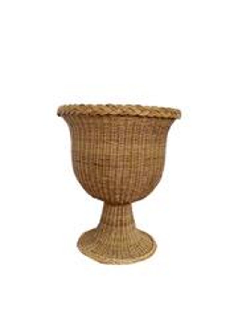 May include: A woven wicker planter with a pedestal base. The planter has a wide, fluted top and a textured, basket-weave design. The natural brown color of the wicker adds a rustic touch. The planter stands approximately 24 inches tall.