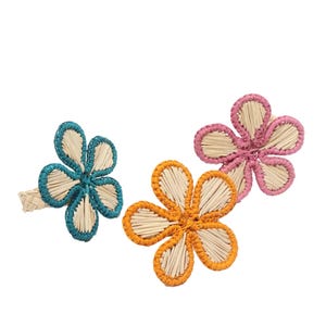 Pode incluir: Três anéis de guardanapo em forma de flor feitos de palha natural trançada. Cada flor apresenta um centro de pétalas de palha bege claro delineadas com fio vibrante nas cores azul-petróleo, laranja e rosa. A base é de palha trançada.