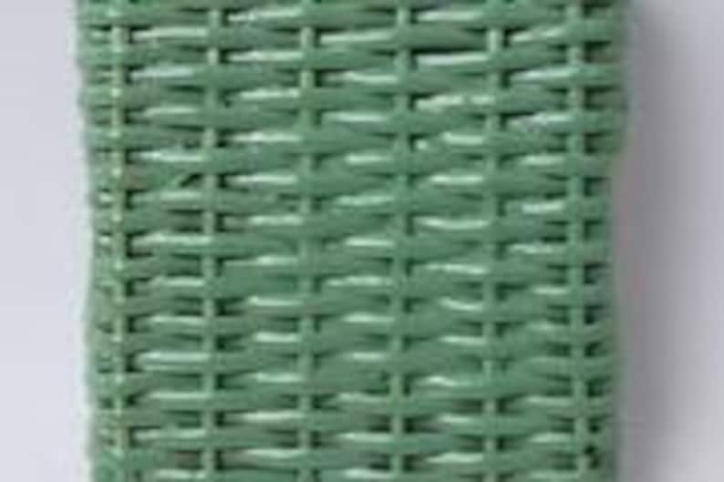 May include: Close-up of a rectangular, woven basket in a muted green color. The basket's texture is created by the interwoven pattern of the material. The basket is likely made of wicker or a similar material. The basket is empty.