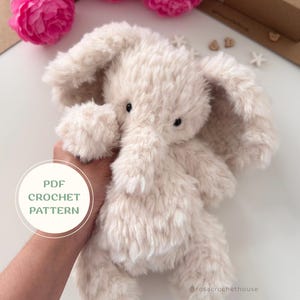 May include: A plush, cream-colored stuffed elephant toy with soft, shaggy fur, large floppy ears, and small black bead eyes. A circular graphic overlay on the left side displays the text PDF CROCHET PATTERN in green lettering.