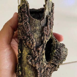 Può includere: Ornamento decorativo per acquario a forma di tronco d'albero invecchiato. Il tronco artificiale è marrone, con accenti verdi e gialli, un interno cavo e un foro laterale.