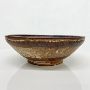 May include: A brown and white ceramic bowl with a wide rim and a slightly flared base. The bowl has a speckled glaze with brown and white streaks.