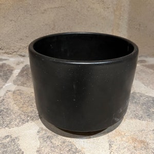 May include: A black ceramic planter with a rounded base. The planter is empty and has a smooth, matte finish.