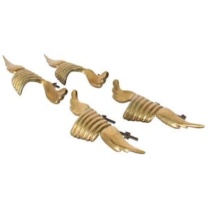 May include: Set of four gold-toned metal drawer pulls with a winged design. Each pull has a curved shape and a detailed wing design.