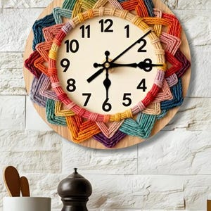 Może przedstawiać: Okrągły drewniany zegar ścienny z kremową tarczą i czarnymi cyframi. Zegar otoczony jest kolorowym, tkanym, geometrycznym wzorem w odcieniach czerwieni, pomarańczy, żółci, zieleni, niebieskiego i fioletu. Wskazówki zegara są czarne.