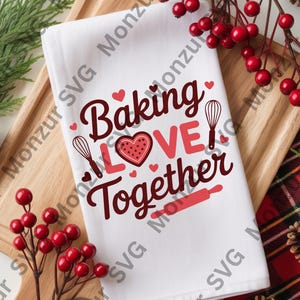 May include: White kitchen towel with the words "Baking Love Together" in red script and a heart-shaped cookie design. The towel also features a whisk and rolling pin graphic. The towel is on a wooden tray with red berries and pinecones.