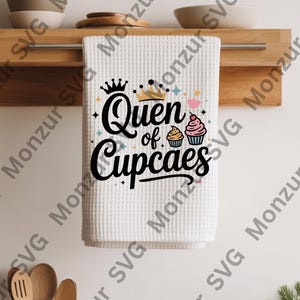 May include: White waffle-weave kitchen towel with the text "Queen of Cupcakes" in black script, adorned with a crown and cupcake illustrations. The towel is hanging on a wooden rack, perfect for a baking enthusiast.