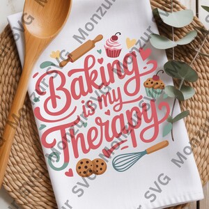 May include: White kitchen towel with the phrase "Baking is my Therapy" in red script. The towel features illustrations of baking tools and treats, including a rolling pin, cupcakes, and cookies. A wooden spoon rests on a woven placemat.