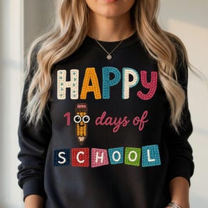 May include: Black sweatshirt with the words "HAPPY 100 days of SCHOOL" in colorful, textured lettering. A smiling pencil graphic is between "HAPPY" and "days". The sweatshirt is a crew neck style.
