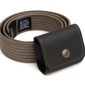 May include: A tan nylon belt with a black leather case. The belt is rolled up and the case is closed with a silver snap. The case has white stitching around the edges. The belt has a small tag with text.