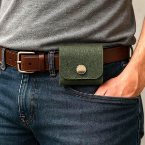 Puede incluir: Un cinturón de cuero marrón con una hebilla plateada y una bolsa de tela verde unida a él.