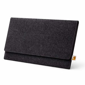 May include: A dark gray felt laptop sleeve with a flap closure. The sleeve has a rectangular shape and a small, rectangular pocket on the front. A small tag is attached to the bottom right corner.