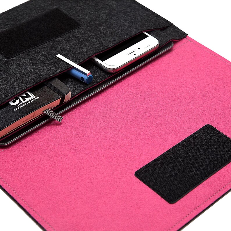 May include: A felt laptop sleeve in gray and pink, with a black Velcro closure. The sleeve has a pocket containing a smartphone, a pen, and a black notebook with the text "CN CARTOON NETWORK".